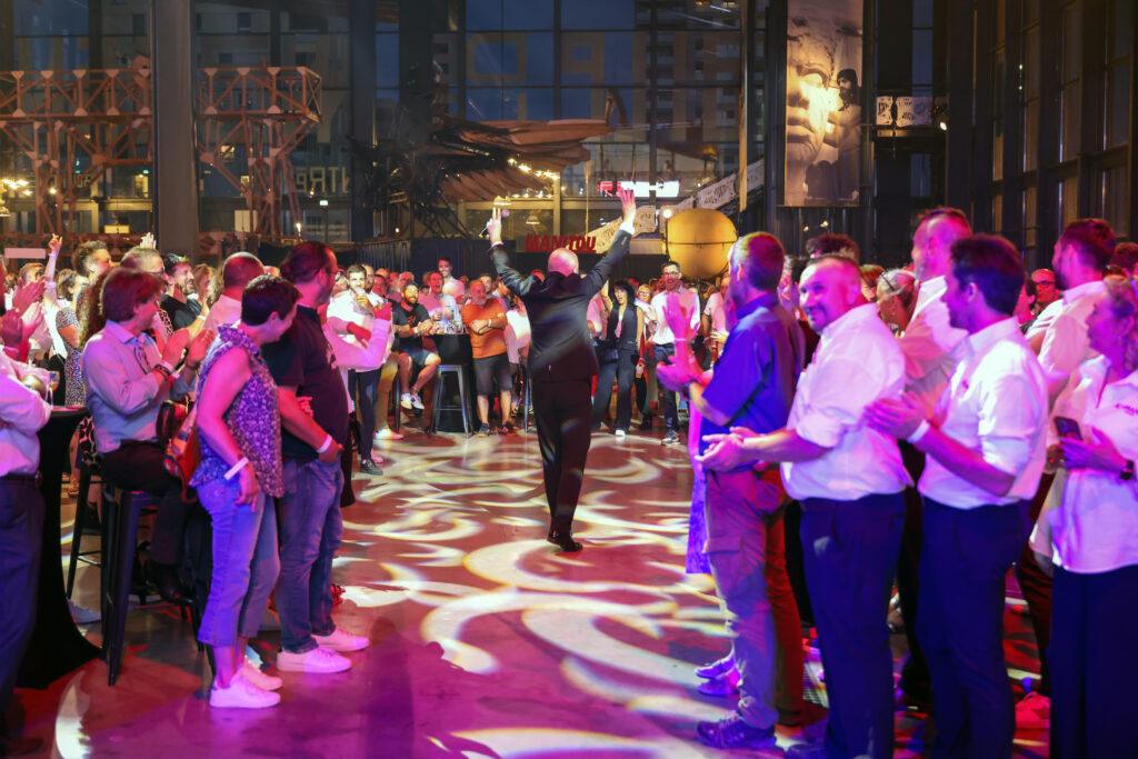 Les 20 ans d’ACTIMAN en images par CHA production Photo de la soirée des 20 ans d’ACTIMAN à la Halle de La Machine à Toulouse, entourés de clients et partenaires, capturant un moment de convivialité et de célébration.